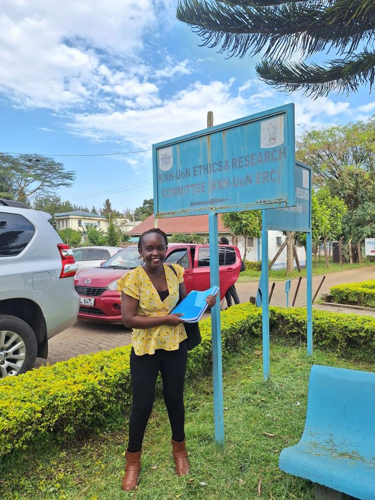 Grace Soma stands in front of a sign at a medical building in Kenya