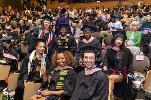 Group shot of DGH graduates wearing black graduation gowns and hats while sitting in the Kane Hall auditorium.