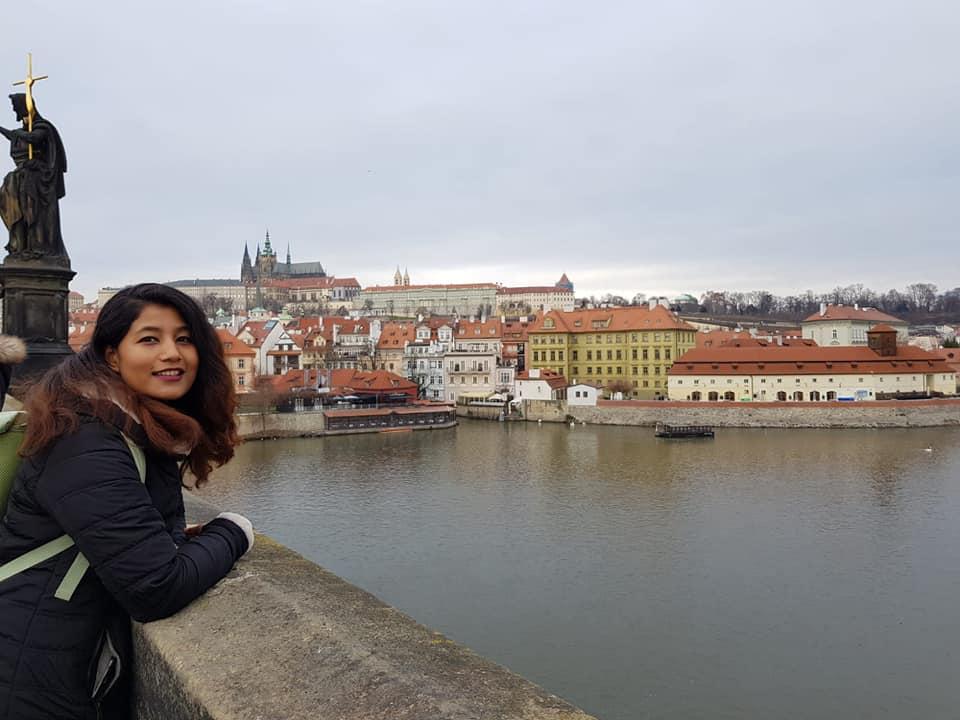 Priyanka Shrestha standing on a bridge in front of historic buildings